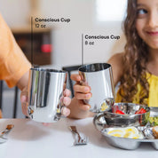 Two kids with Conscious Cups, on the left side the 12 ounce stainless steel shiny cup and on the right side an 8 ounce stainless steel cup reflecting the child's food. 