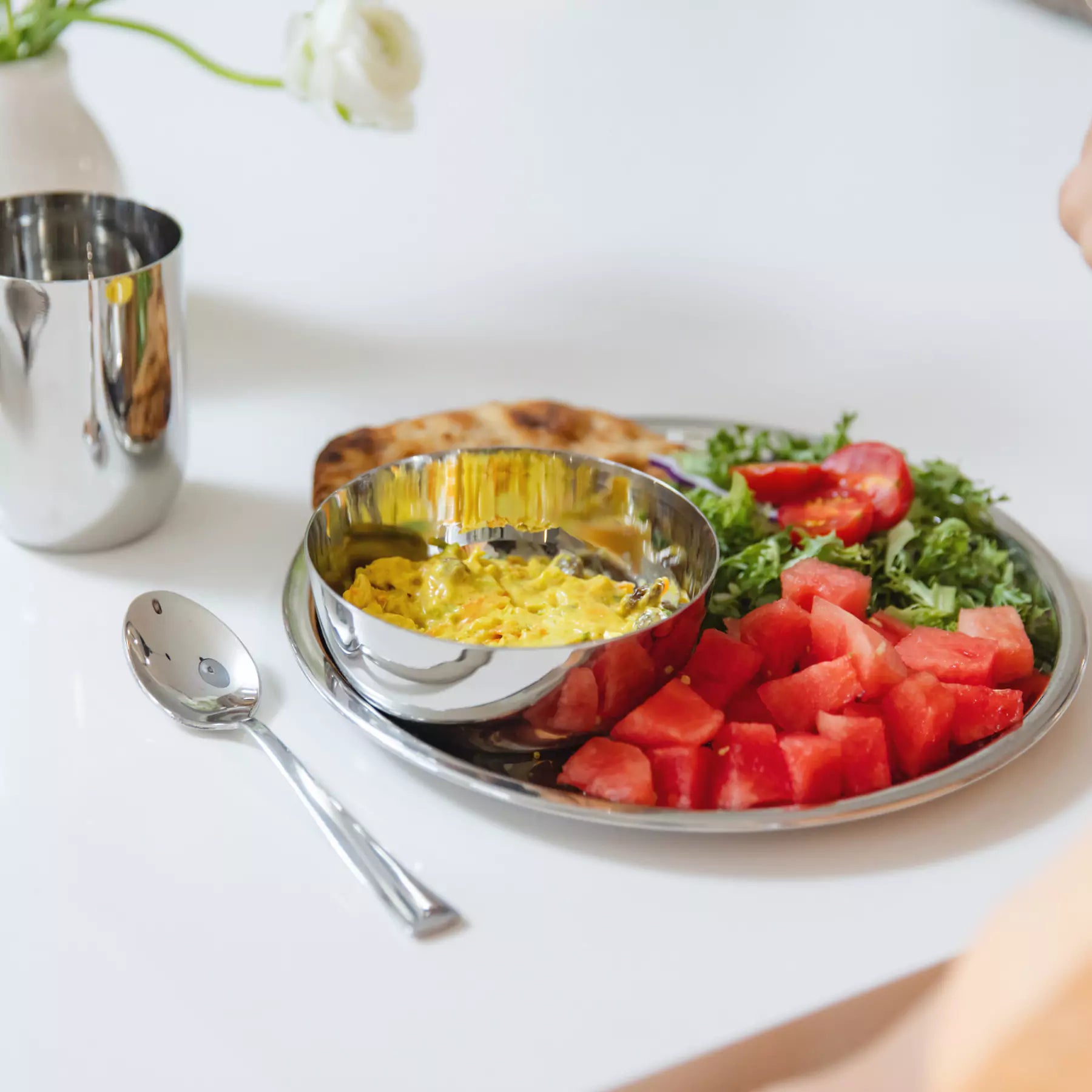 Classic stainless steel plate and 14 ounce bowl with scrambled eggs, watermelon, and salad on a white table with spoon 