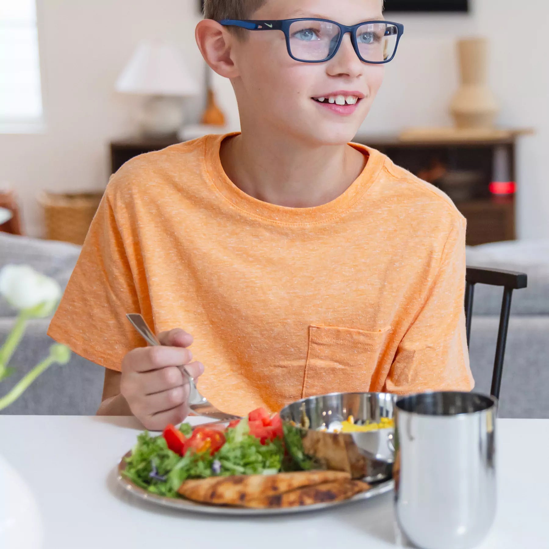 Older boy eating salad with tomatoes and pita on Ahimsa's Purposeful Portions Set which includes a 9 inch stainless steel plate (no compartments), 14 ounce stainless steel bowl, 12 ounce stainless steel cup, fork, and spoon - the perfect set for older kids to adults
