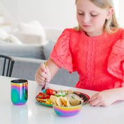 Child eating meal at the table - using a beautiful, rainbow, stainless steel meal set - bowl, cup, plate, fork, and spoon